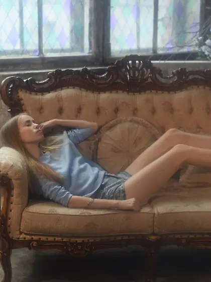 Really skinny blonde with longish legs posing on a chic sofa Vid
