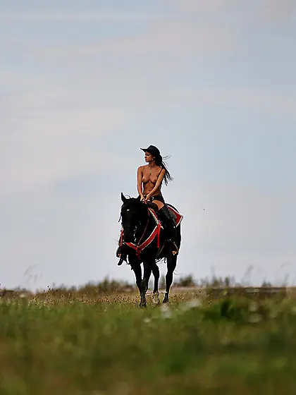 Melisa Mendiny rides her strong black horse outdoors wearing not