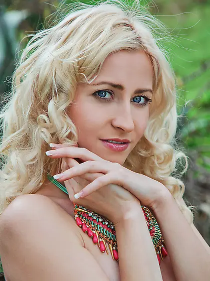 Blue-eyed blonde with wavy hair shows her trimmed pussy outdoors