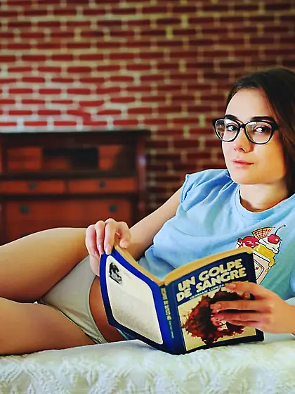 Insatiable teenager with sexy legs reads a book and shows a hole