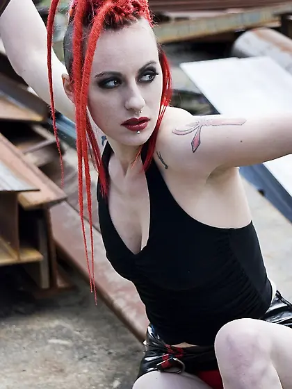 Tattooed emo girl with red dreadlocks poses naked in an industri