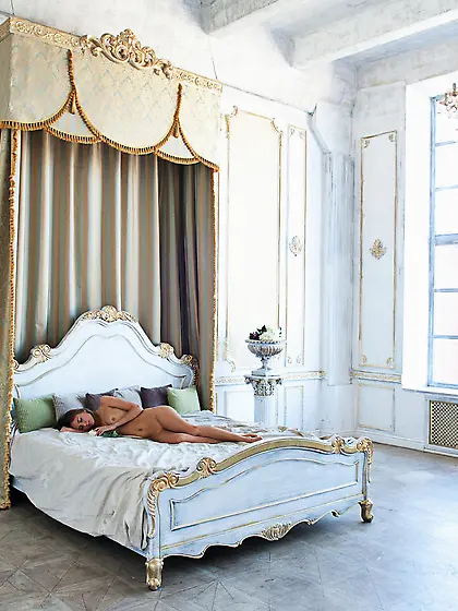 Luxurious brunette with blue eyes laying naked on a massive bed