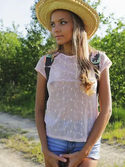 Hat-wearing blonde checks out some flowers while completely nake