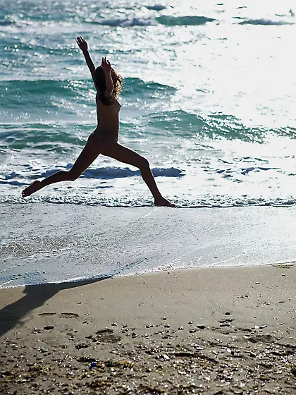 Playful beach dweller shows off her young nude body by the water