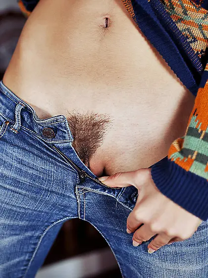 Youthful brunette in skinny jeans shows her bushy pussy on a sof